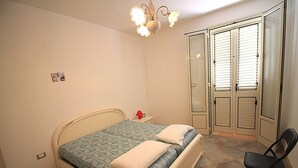 Een slaapkamer met een bed, nachtkastje, stoel en een kledingkast.