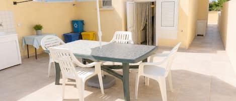 Une terrasse extérieure avec une table et des chaises, un parasol à rayures et une petite table sur laquelle est posée une plante.