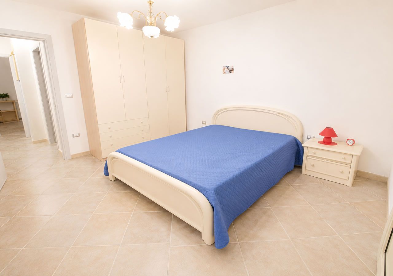 A bedroom with a bed, a wardrobe, a nightstand, and a red lamp.