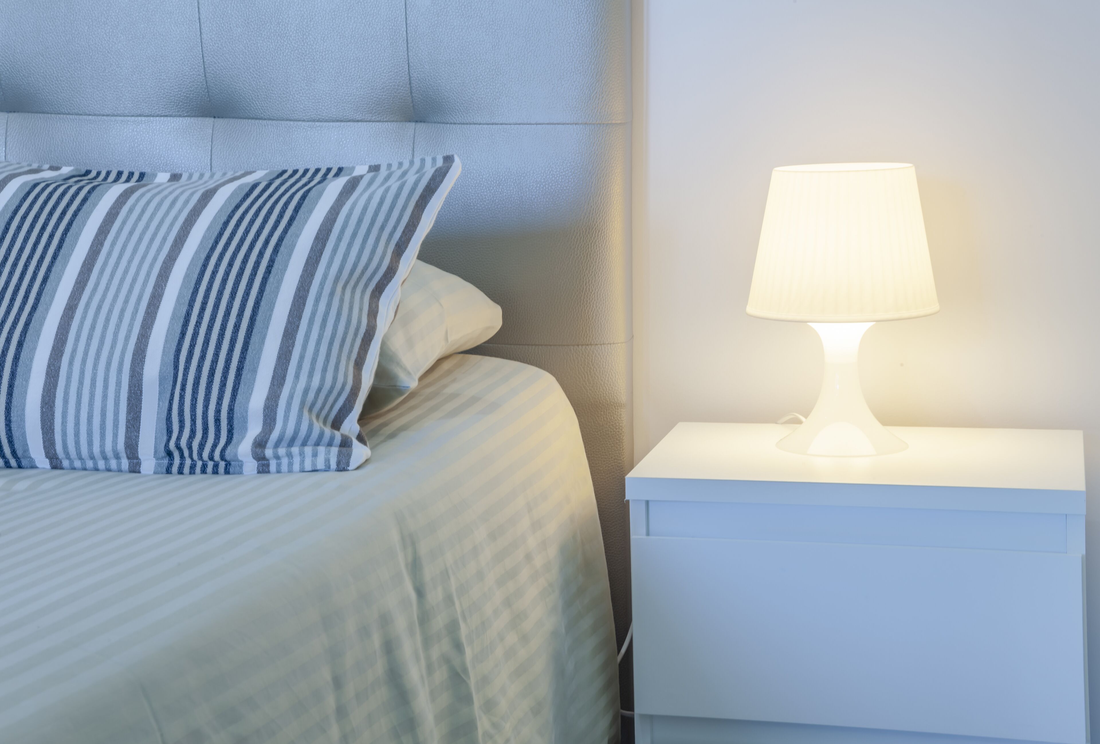 En pænt redt seng med stribede puder, et hvidt natbord og en hvid lampe.