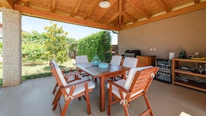 An outdoor patio with a wooden table and chairs, a grill, and a wine cooler. - Apartments Neva, (15356), Štinjan, hr (Štinjan)