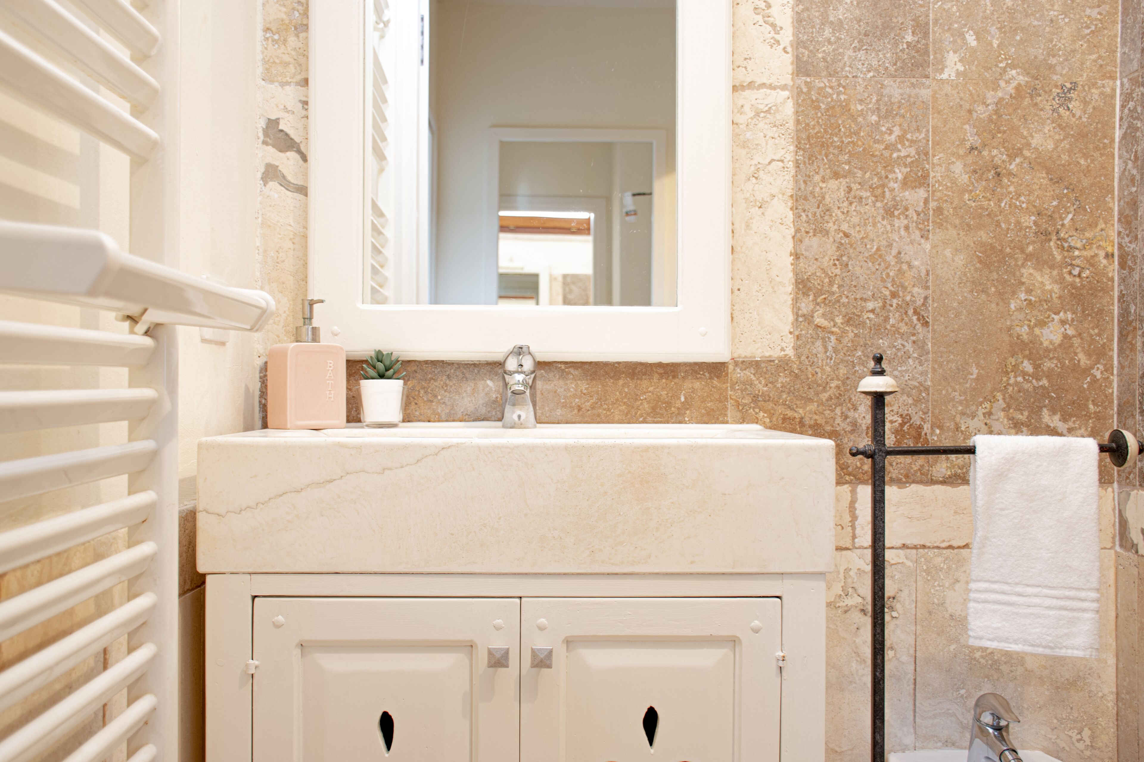 A bathroom with a marble sink, a mirror, a towel rack, and a radiator.