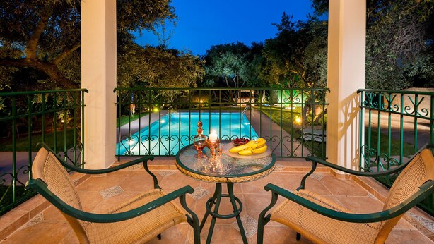 Un patio al aire libre con piscina, mobiliario de mimbre y una mesa con fruta y una vela.