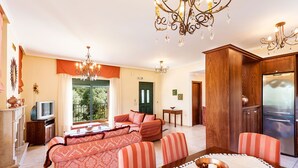 Amplia sala de estar con un conjunto de sofás, una mesa de comedor con un frutero y una cocina moderna con refrigerador.