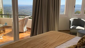 Ein Schlafzimmer mit einem großen Bett, Blick auf die Landschaft durch eine Schiebetür und einem Sessel am Fenster.
