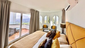Ein Schlafzimmer mit einem großen Bett, zwei Sesseln, einem Tisch und Blick ins Freie.