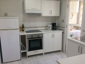 A compact kitchen with white cabinets, a built-in oven, a stove, and a coffee maker.