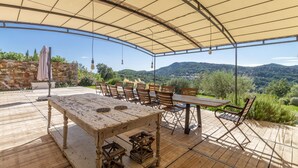 An outdoor patio with a wooden table and chairs, a stone wall, and a view of the countryside. - This place is magic in the wonderful village of La Garde Freinet. (La Garde-Freinet)