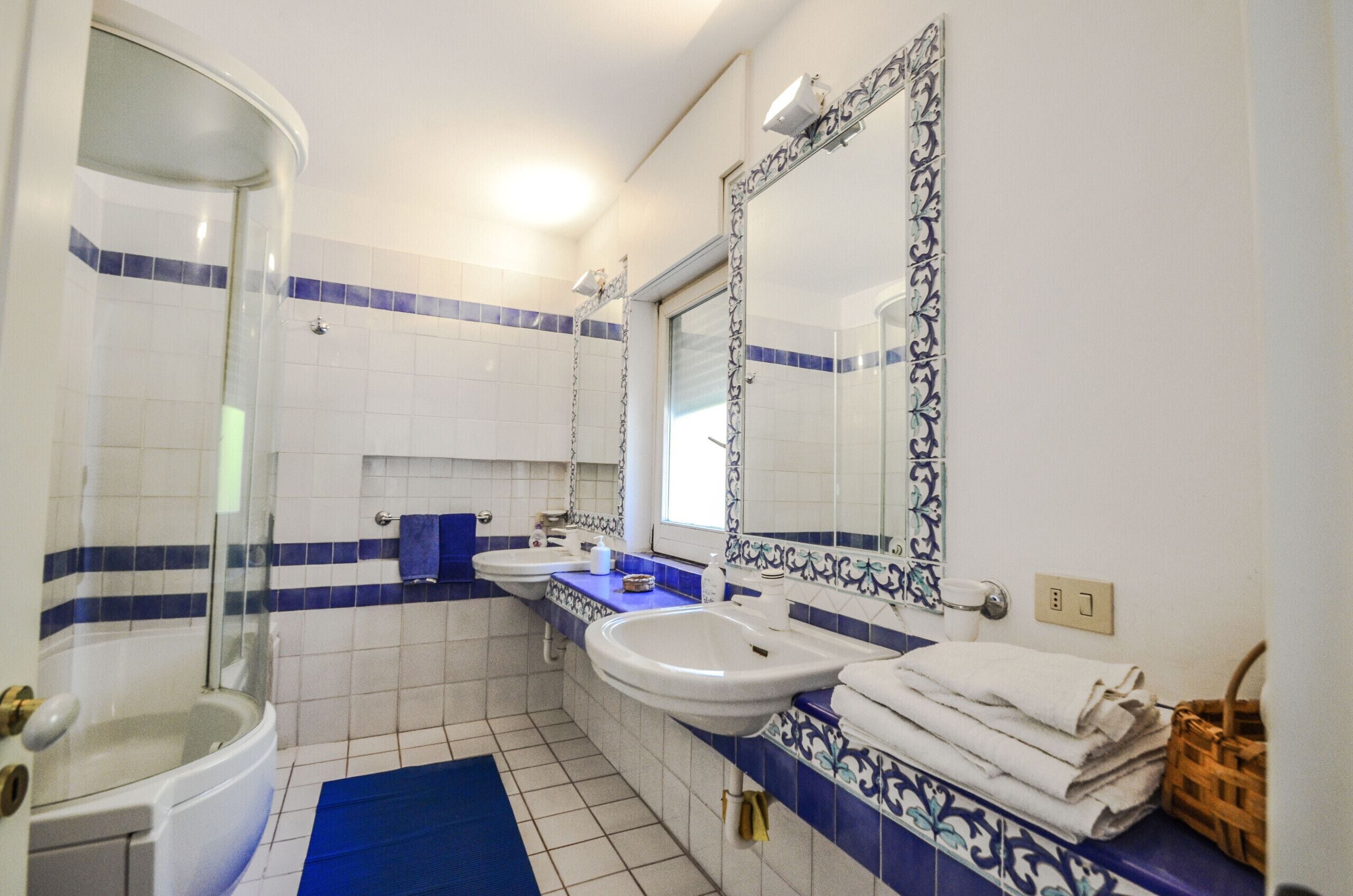 Une salle de bain dotée d’une douche à parois de verre, de deux lavabos et d’un grand miroir orné de carreaux décoratifs.