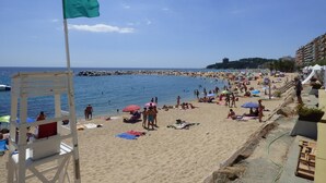 A beach with a lifeguard tower, umbrellas, and people sunbathing. - Casa Oasis, Calonge - Costa Brava (Calonge)