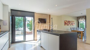 A modern kitchen with a central island, a dining area with a table and chairs, and a large window providing natural light. - Casa Oasis, Calonge - Costa Brava (Calonge)