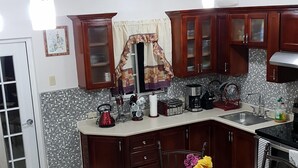 A kitchen with a central island, wooden cabinets, a tiled backsplash, and a dining area with a glass table and chairs. - Kensington Oasis 2b/3bth- New Kingston (24 hrs security, free wifi, hot water) (New Kingston)