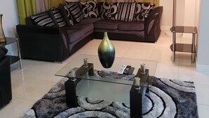A living room with a sectional sofa, a glass coffee table, a floor lamp, and a patterned rug. - Kensington Oasis 2b/3bth- New Kingston (24 hrs security, free wifi, hot water) (New Kingston)