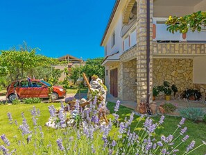 A house with a stone facade, a red car parked in the driveway, and a garden with lavender flowers. - Apartments Blanka, (14958), Privlaka, hr (Privlaka)