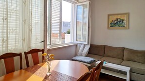 Une pièce comprenant une table à manger, des chaises, un canapé, un radiateur et une fenêtre avec des stores.