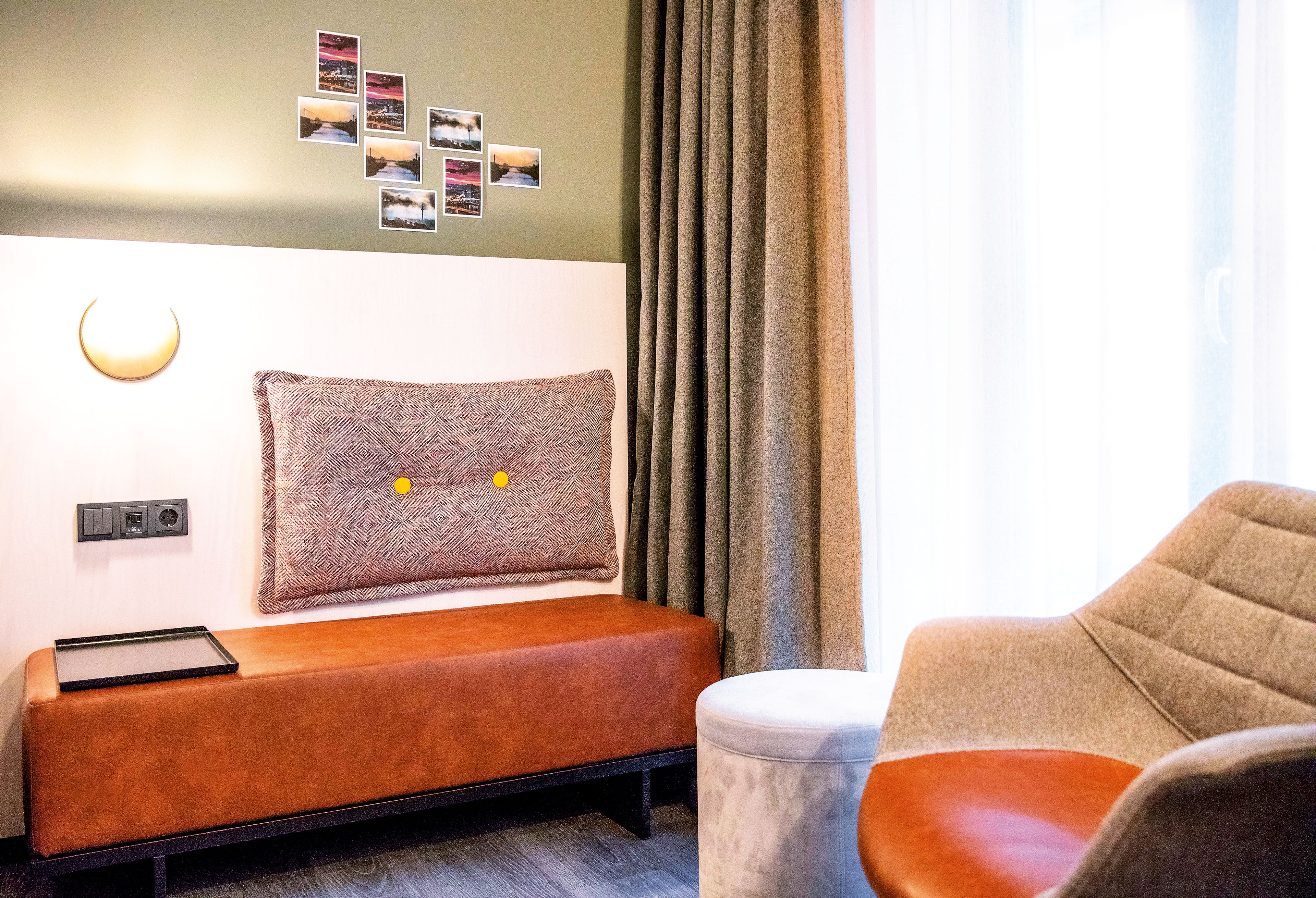 Una habitación moderna con una cama, un banco, una silla y una lámpara fijada a la pared.