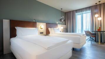 Habitación de hotel con dos camas, un escritorio y una silla, y un ventanal con cortinas.