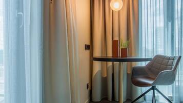 Ein Zimmer mit einem runden Tisch, einem Stuhl, einer Topfpflanze und Vorhängen.