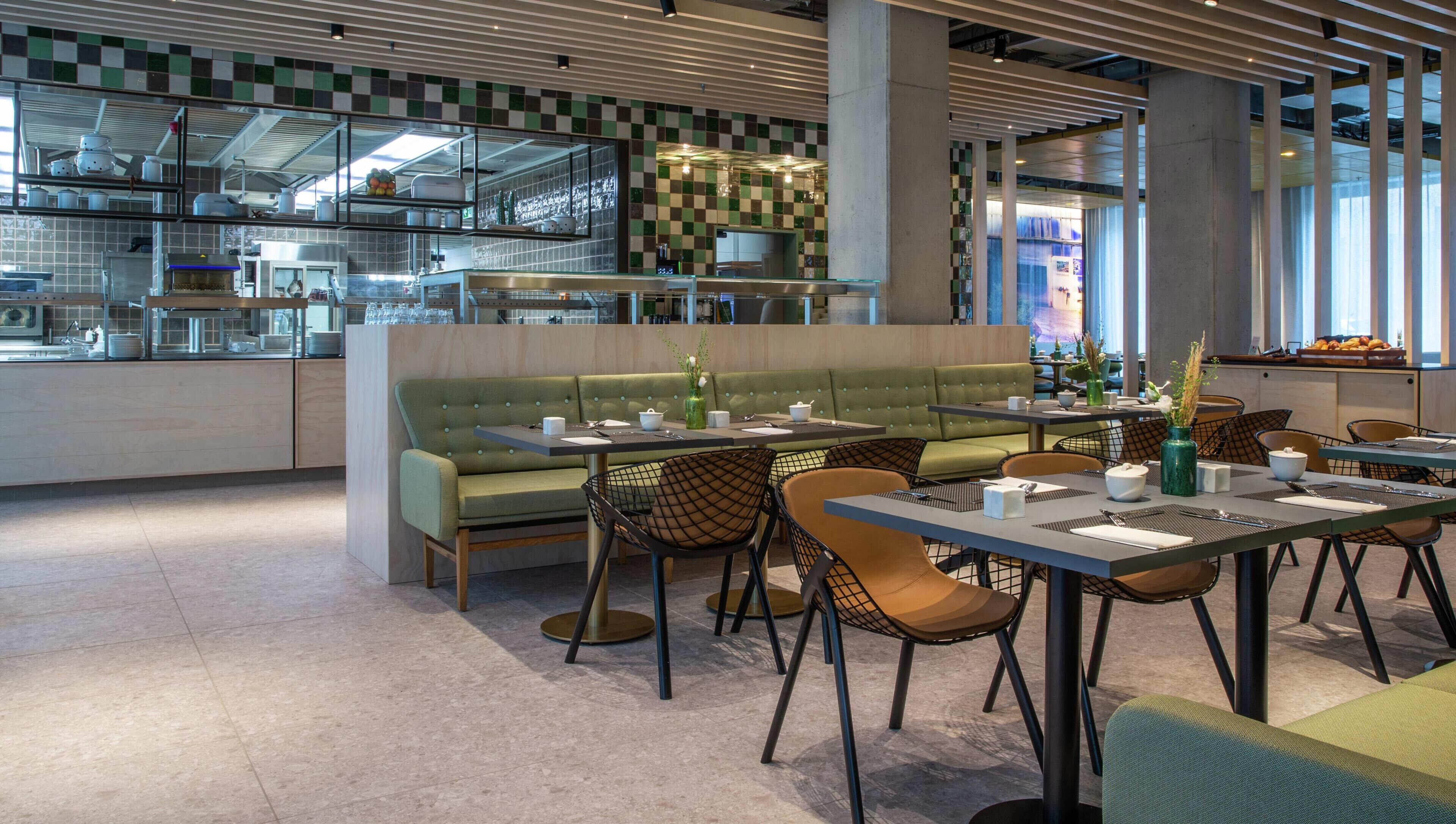 Un interior de restaurante moderno con un sofá verde, sillas negras y marrones, y un salpicadero de azulejos.