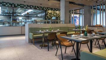 Un interior de restaurante moderno con un sofá verde, sillas negras y marrones, y un salpicadero de azulejos.