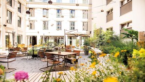 Un patio al aire libre con mesas y sillas, rodeado de plantas y flores.