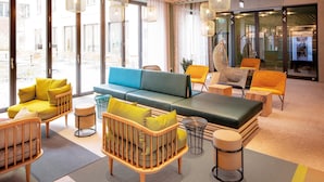 Un moderno vestíbulo de hotel con un sofá verde, sillas amarillas y anaranjadas, y una cuna de madera.
