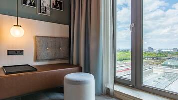 A modern room with a bench, ottoman, wall-mounted light, and a city view through large windows.