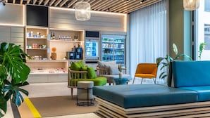 Un área de descanso moderna con asientos, un refrigerador lleno de bebidas y una planta.