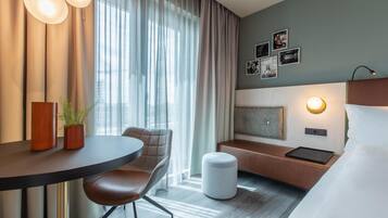 Ein Hotelzimmer mit einem Bett, einem Schreibtisch mit Stuhl, einem kleinen Tisch mit zwei Vasen, einer Bank und einer Wandlampe.