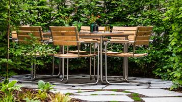 Un patio jardín con una mesa redonda y seis sillas de madera con patas metálicas.