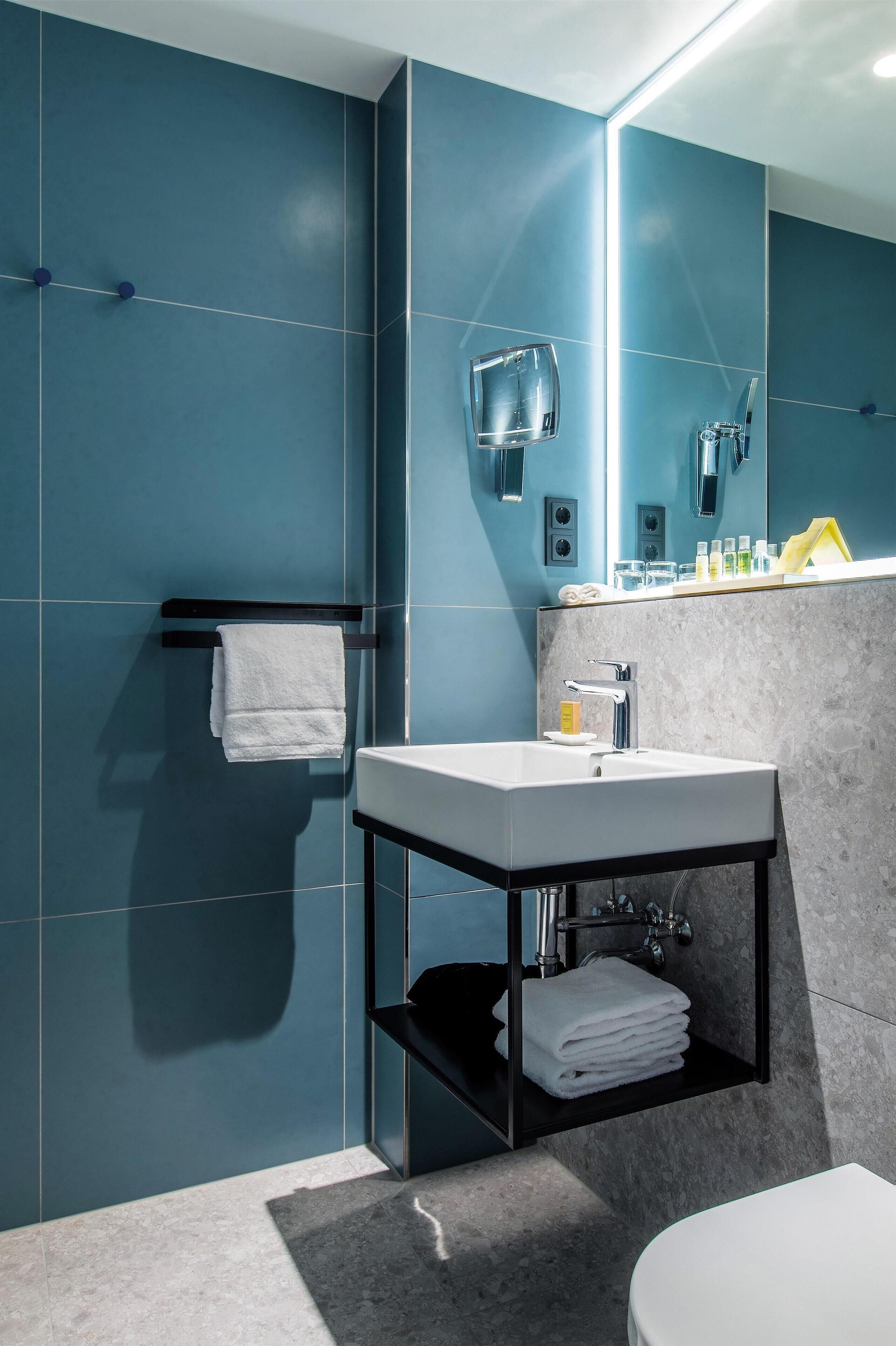 Un baño moderno con un espejo grande, un lavamanos blanco y un perchero para toallas.
