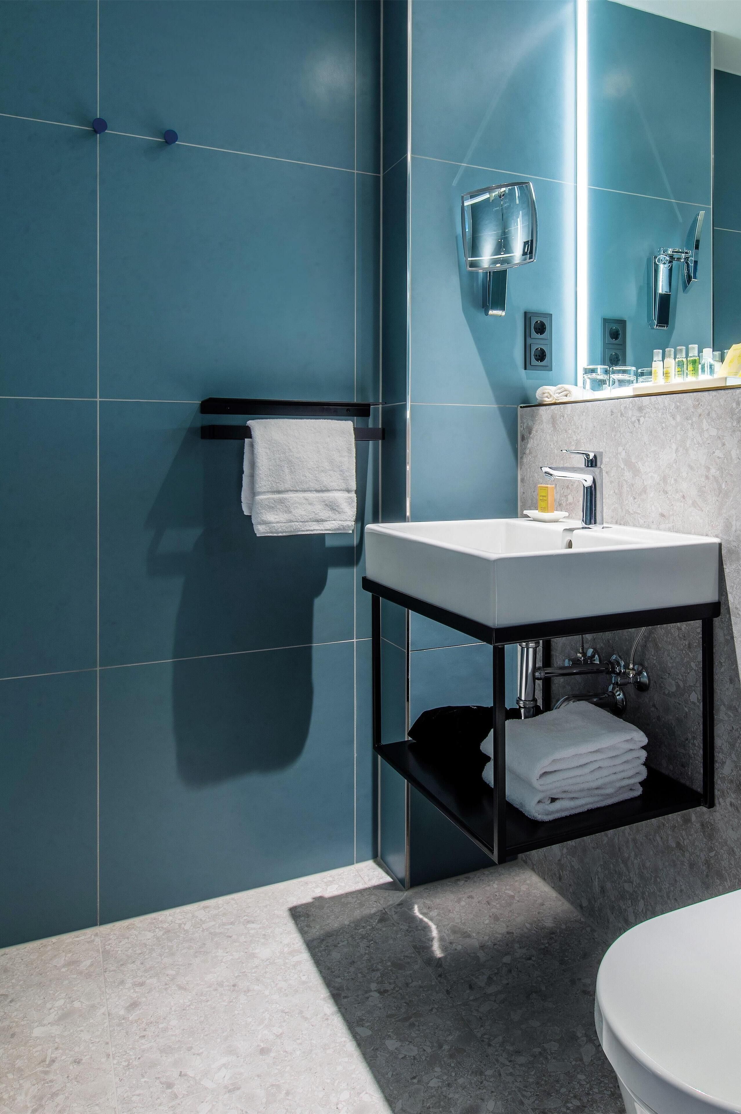 Un baño moderno con un espejo grande, un lavamanos blanco y un perchero para toallas.