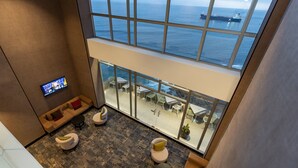 A high-ceilinged lounge area with a large window overlooking the sea, furnished with modern seating and a flat-screen TV. - Hampton by Hilton Antofagasta (Antofagasta)