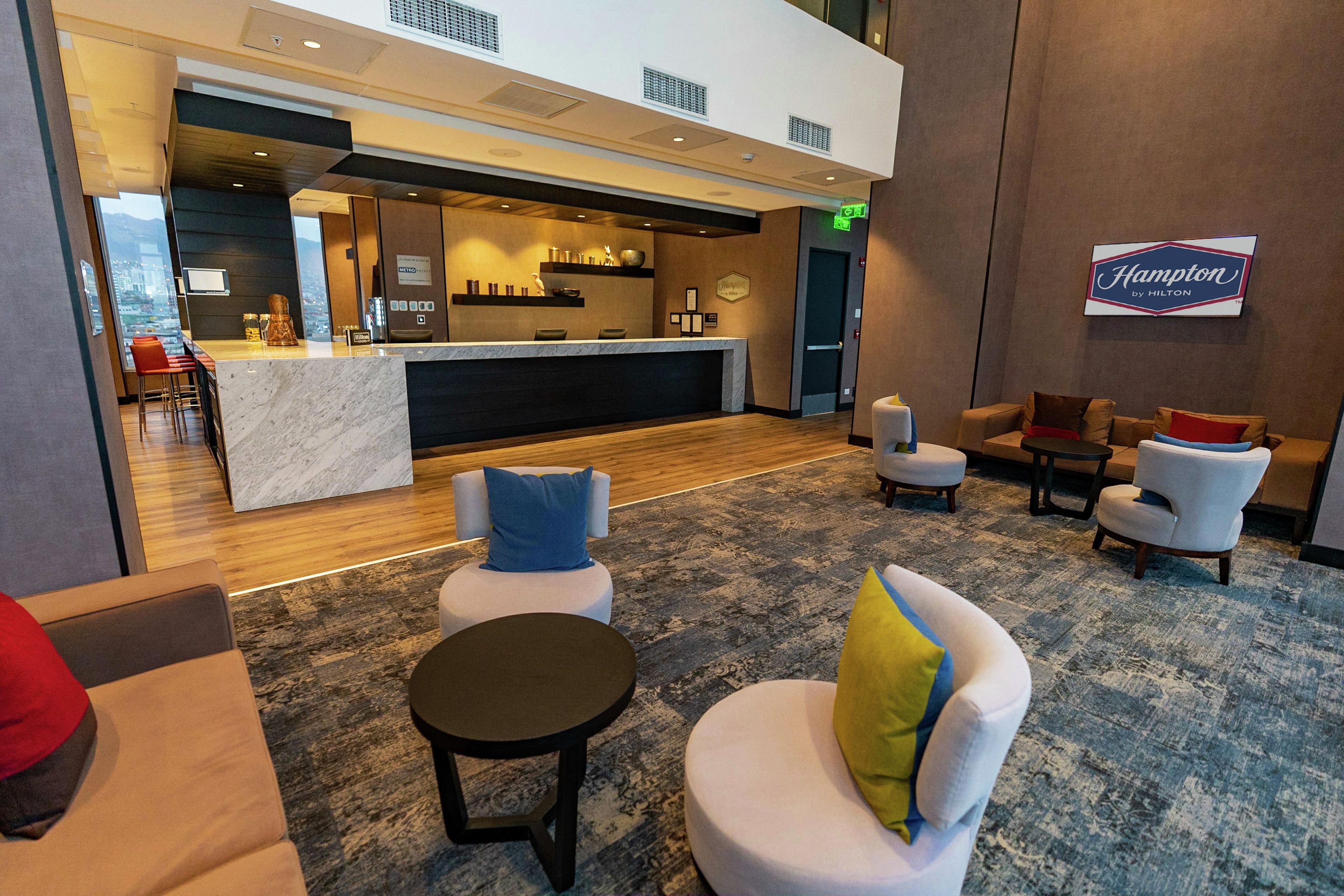 A hotel lobby with a reception desk, seating area, and a Hampton by Hilton sign.