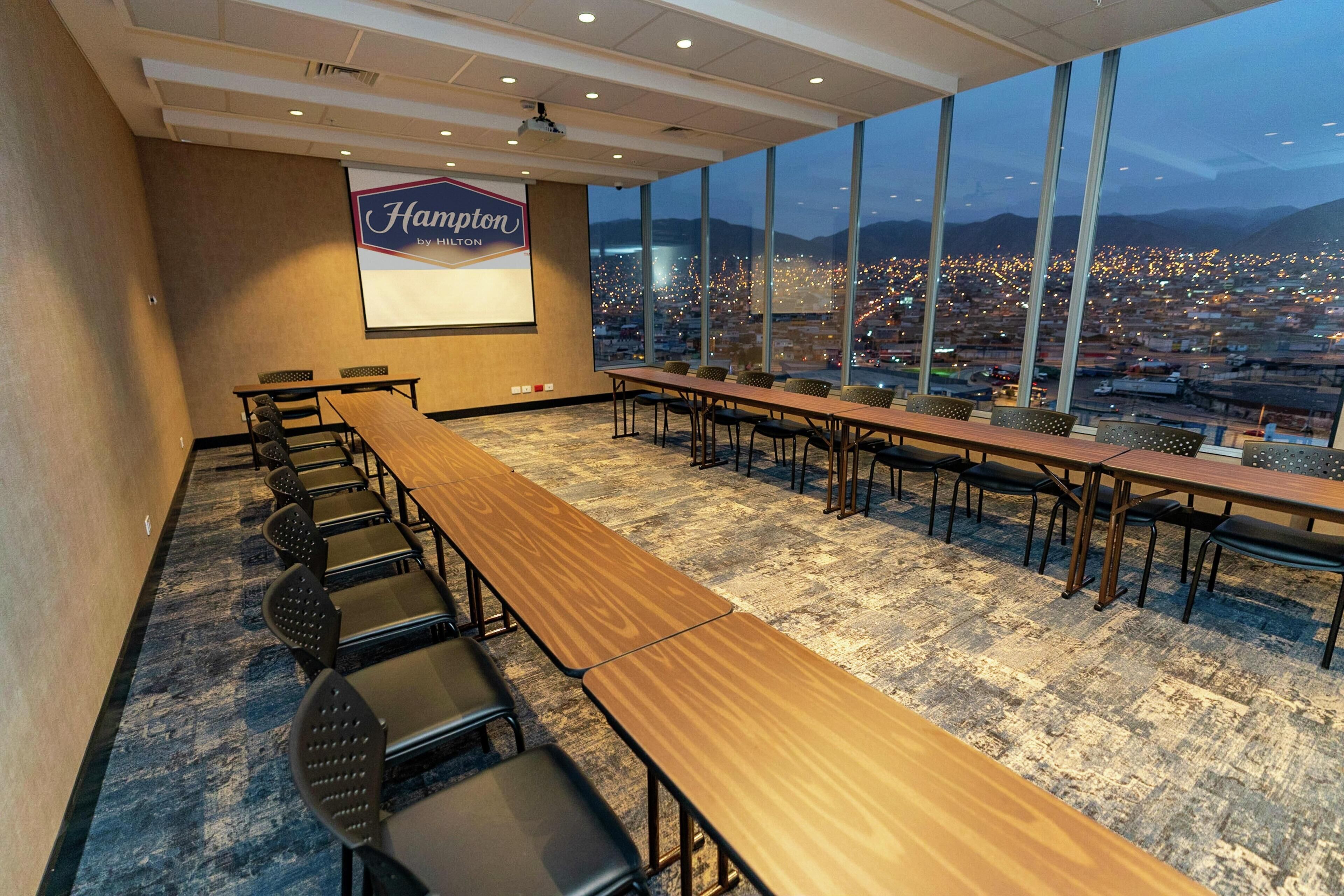Une salle de conférence dotée d’une grande table et de chaises, d’un écran de projection et offrant une vue sur le paysage urbain grâce à de grandes fenêtres.