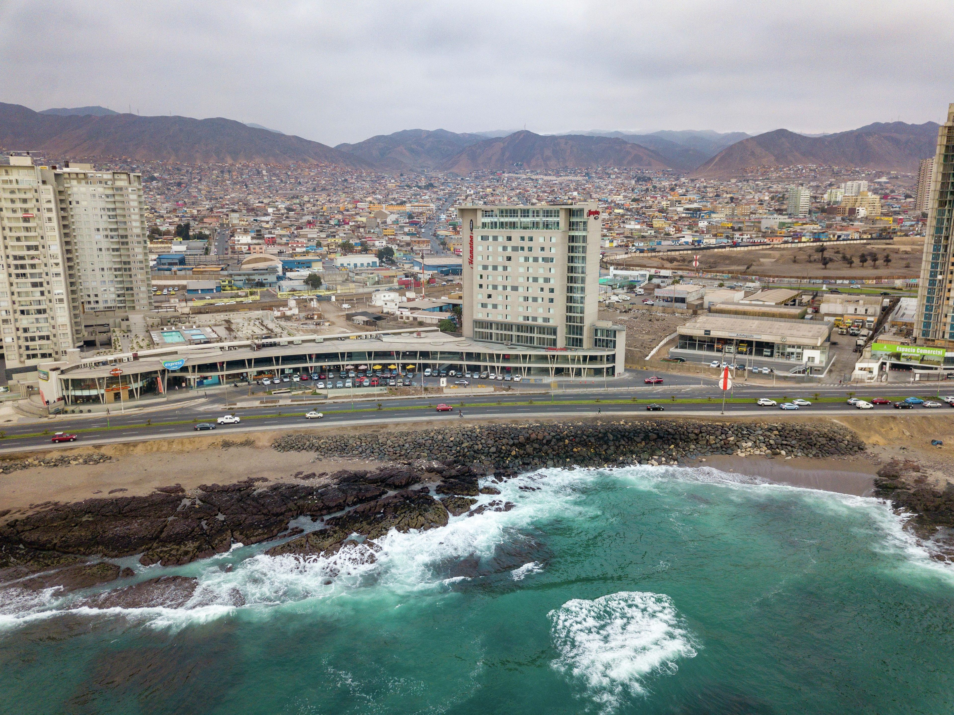 A coastal cityscape with high-rise buildings, a marina, and a rocky shoreline.