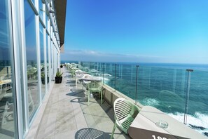 Een balkon met glazen wanden, buitenmeubilair en uitzicht op de oceaan.