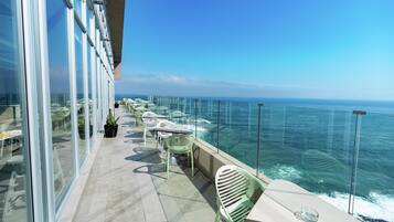 A balcony with glass walls, outdoor seating, and a view of the ocean.