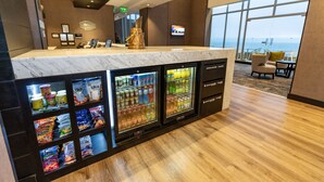 Zona de recepción de un hotel con mostrador de mármol, dispensadores de bebidas y vistas al océano a través de amplios ventanales.