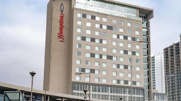 Un hotel con un llamativo letrero de 'Hampton', un diseño arquitectónico moderno y un estacionamiento con coches a la vista.