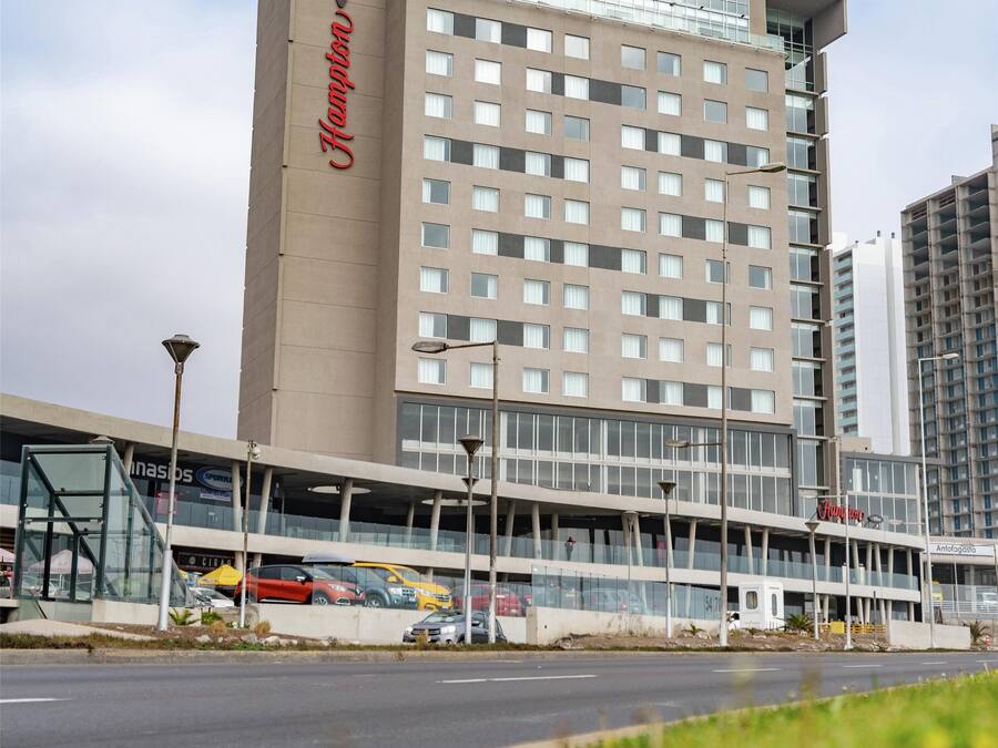 Un hotel con un llamativo letrero de 'Hampton', un diseño arquitectónico moderno y un estacionamiento con coches a la vista.