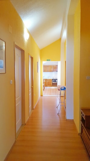Enter a hallway leading to a kitchen area with three doors and a cozy seating nook.