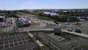 An aerial view of a parking lot with marked spaces, a pedestrian crossing, and a road intersection with traffic lights.