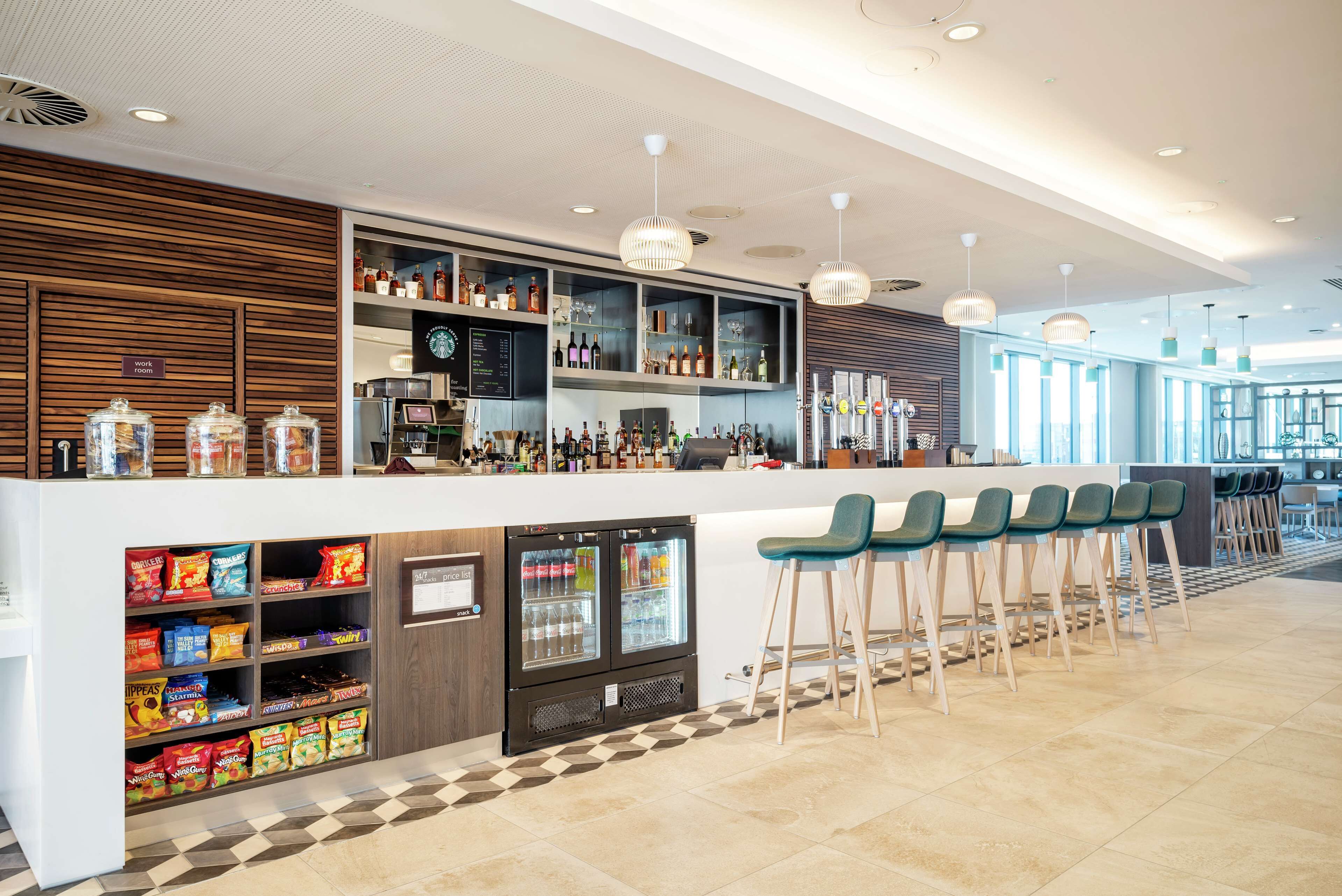 A modern bar area with a checkered floor, a refrigerated display case, and a variety of snacks.