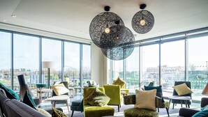 A modern lounge area with large windows, comfortable seating, and unique spherical pendant lights. - Hampton by Hilton Stockton on Tees (Stockton-on-Tees)