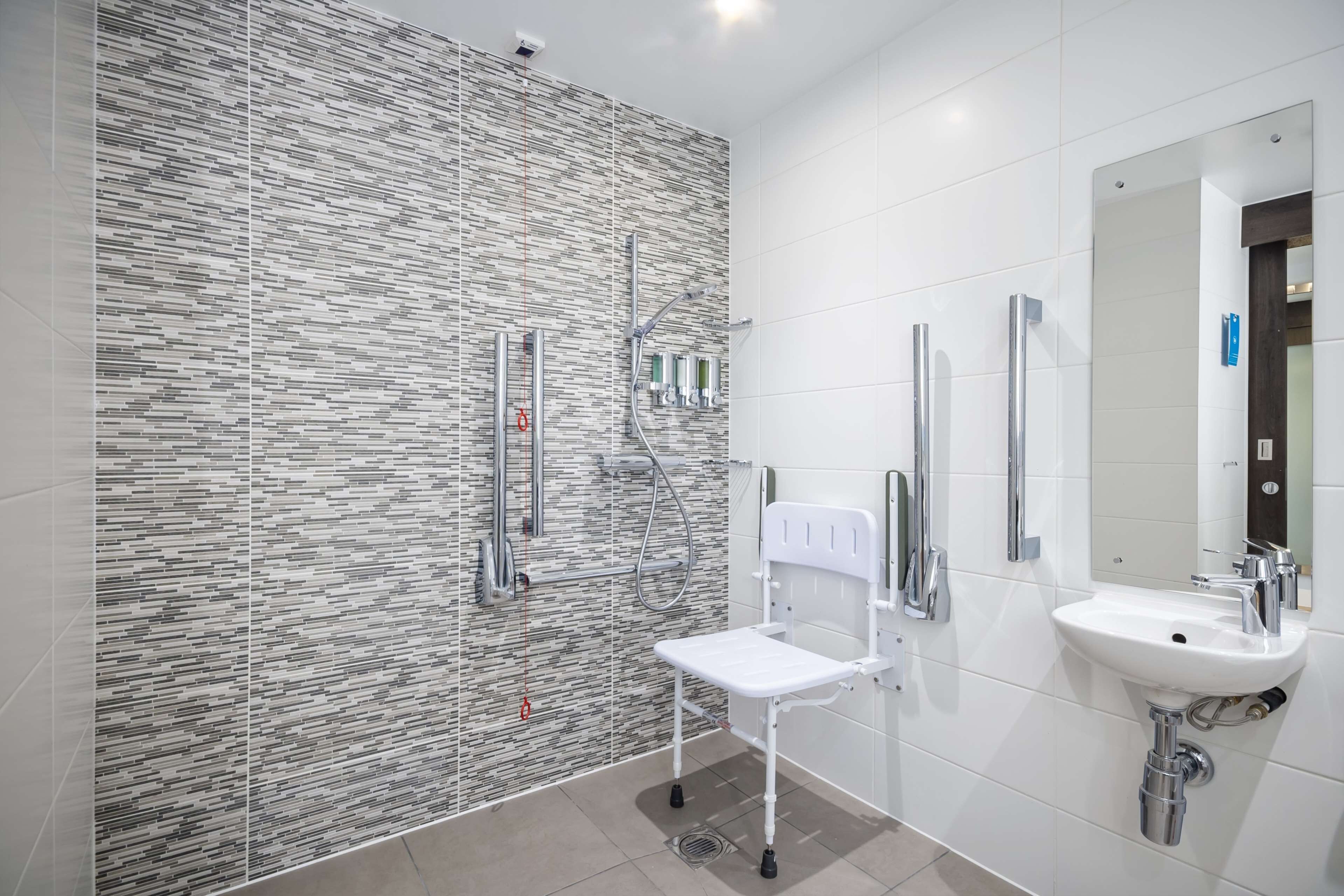 A modern bathroom with a textured wall, a white chair, a sink, and a mirror.