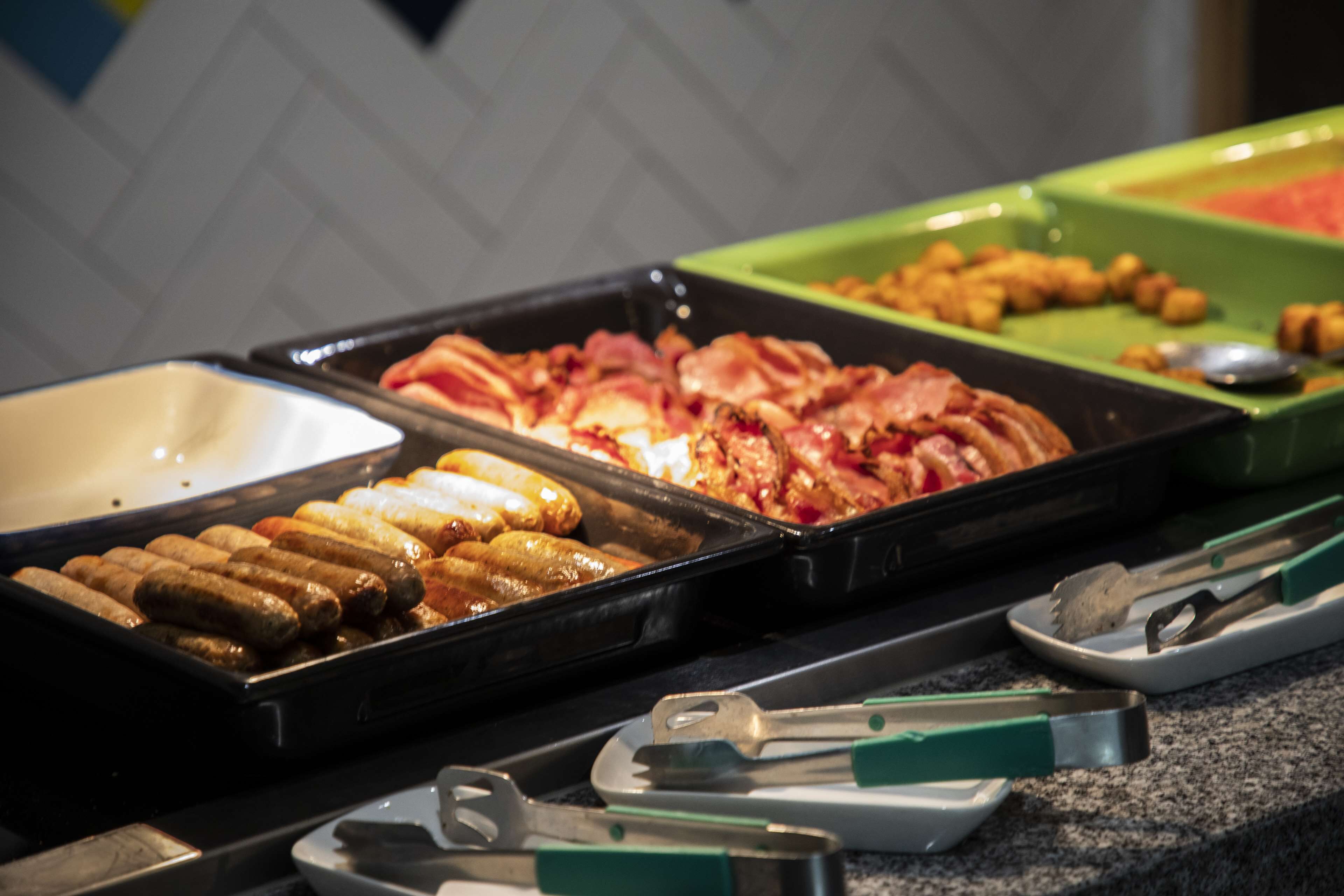 A buffet with various food items including sausages, bacon, and other meats.