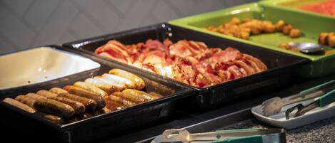 A buffet with various food items including sausages, bacon, and other meats.