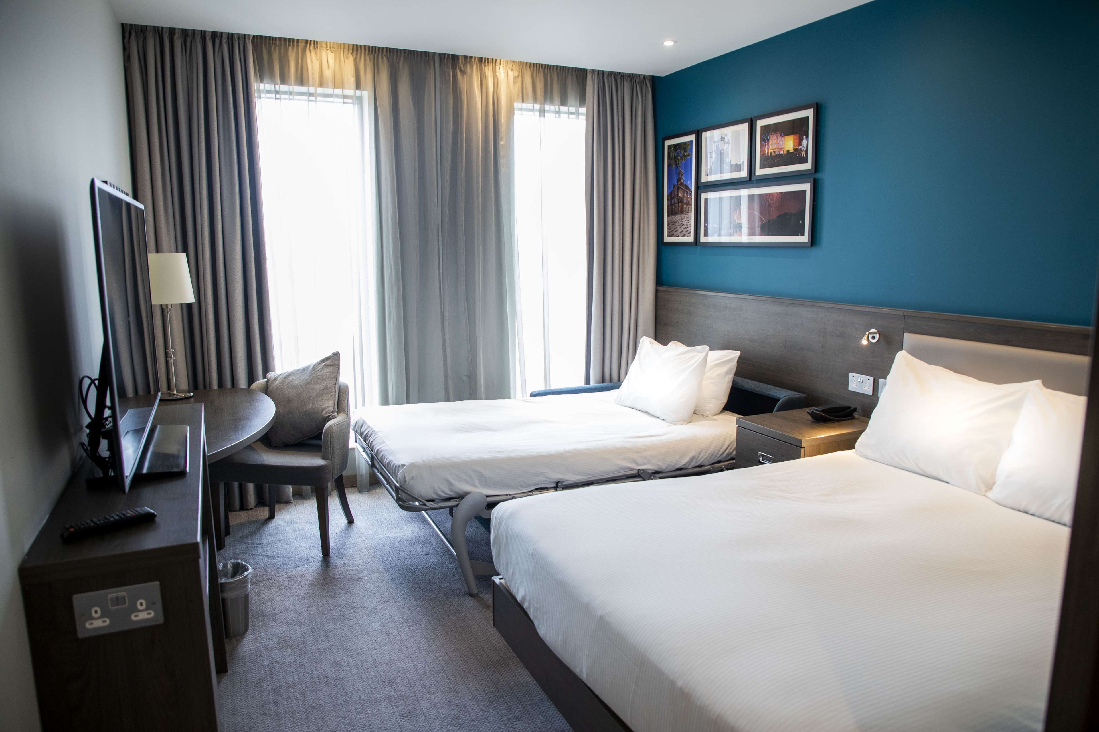 A hotel room with two beds, a desk, a chair, and a TV.