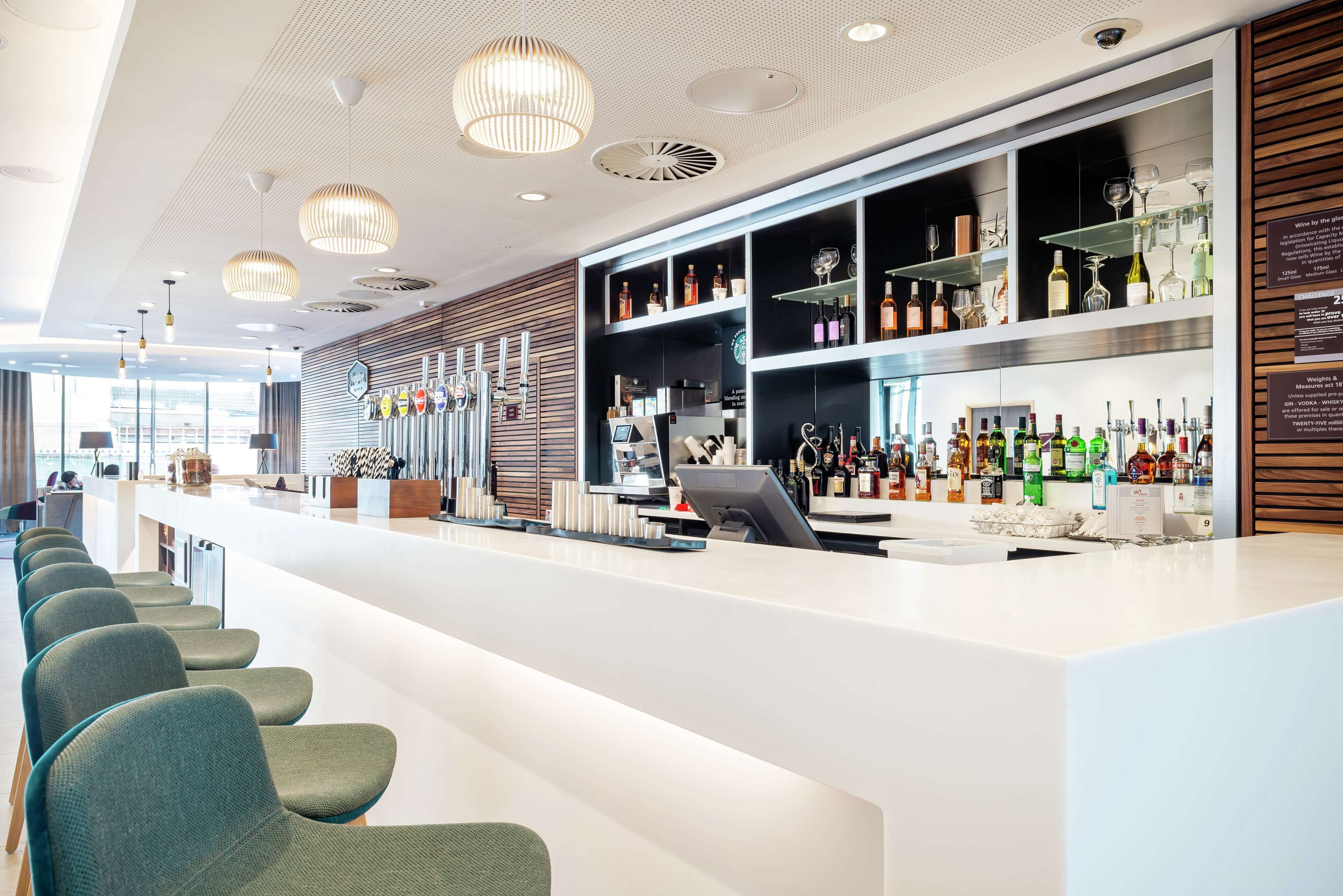 A modern bar area with a long counter, multiple shelves of bottles, and a row of chairs.